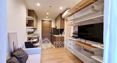 Modern living room with open kitchen, stylish shelving, and cozy seating area in a compact apartment.