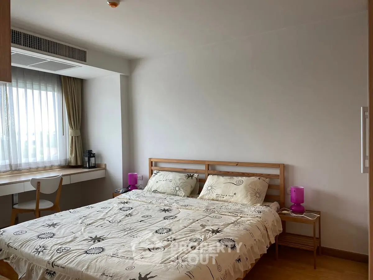Cozy bedroom with natural light, featuring a comfortable bed and a functional workspace.