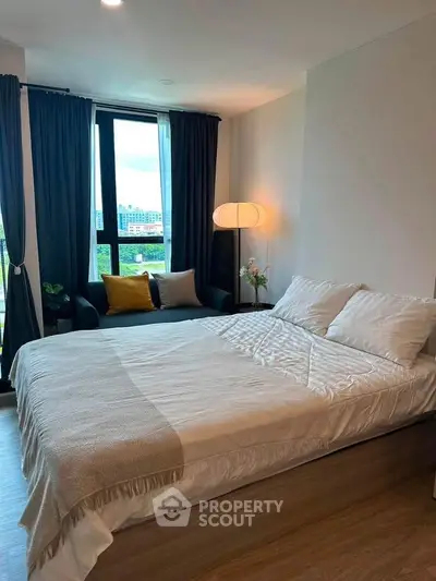 Modern bedroom with cozy bed, stylish lamp, and city view from large window.