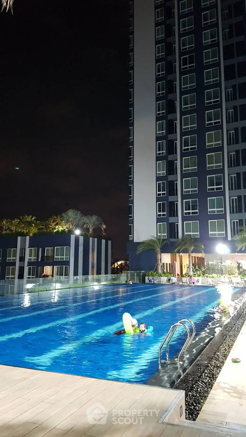 Luxurious high-rise building with illuminated swimming pool at night, perfect for relaxation.