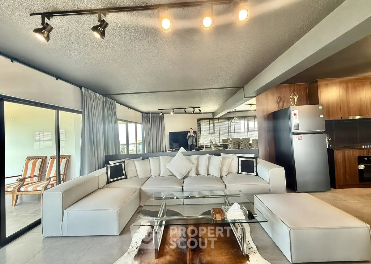 Spacious modern living room with stylish white sectional sofa and glass coffee table, featuring open layout and natural light.