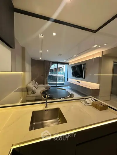 Modern open-plan living room with sleek kitchen and large TV, featuring elegant lighting and contemporary design.