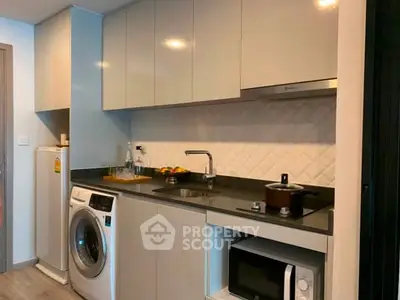 Modern kitchen with sleek cabinets, washing machine, and microwave in a compact layout.