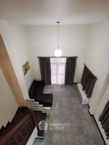 Spacious and well-lit living room with high ceiling, elegant staircase, and large windows draped in stylish curtains.