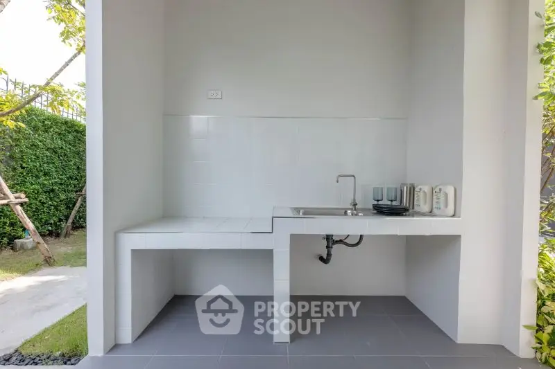 Modern outdoor kitchen with sleek white countertops and lush garden view.