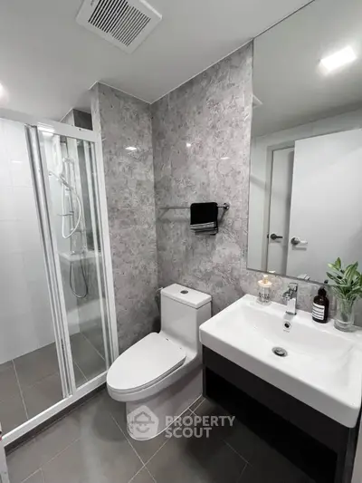 Modern bathroom with sleek fixtures and a glass-enclosed shower, featuring elegant gray tile walls.
