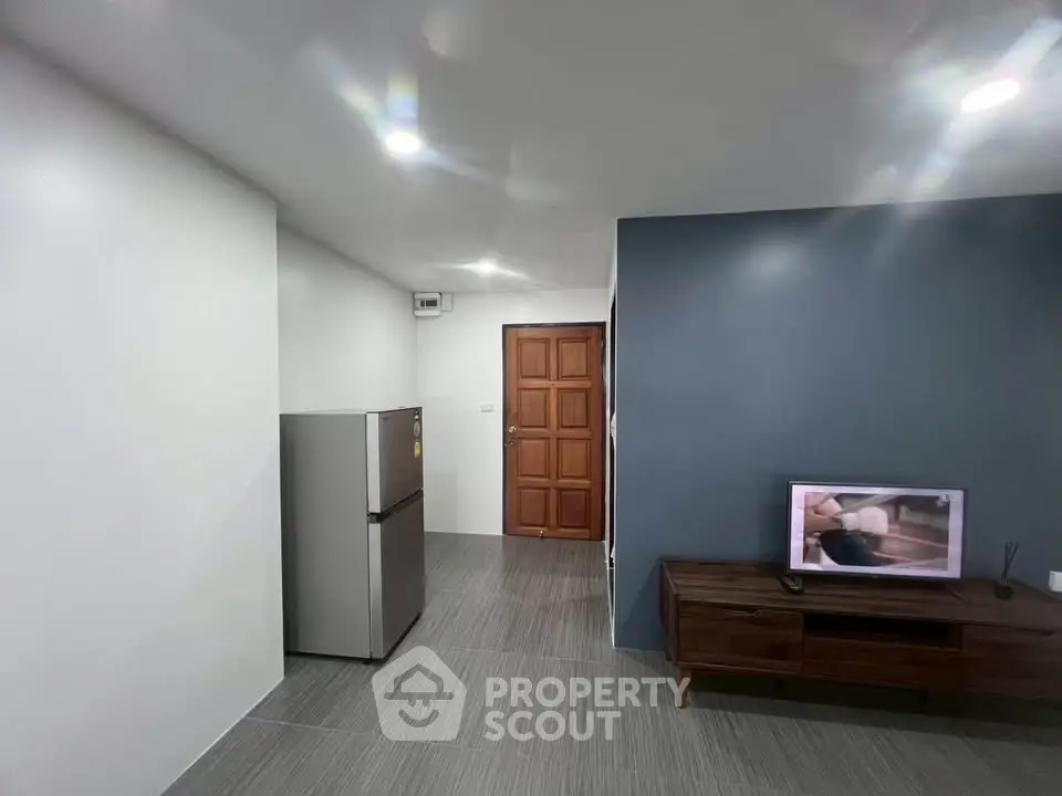 Modern living room with sleek design, featuring a TV and stainless steel fridge, perfect for urban living.