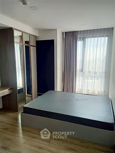 Modern bedroom with large window and wooden flooring in a stylish apartment.