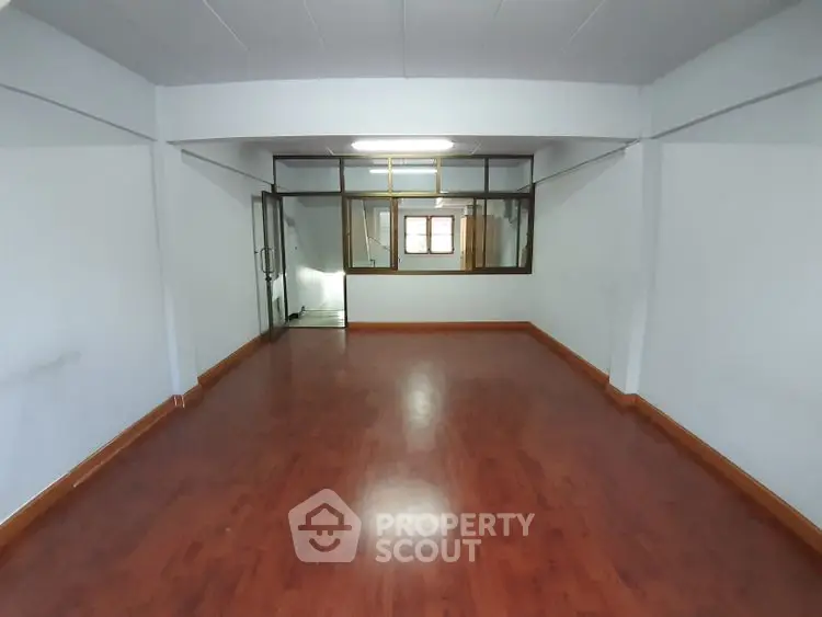 Spacious empty room with wooden flooring and large window, ideal for customization.