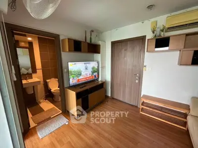 Modern living room with wooden flooring, TV unit, and bathroom access in cozy apartment.
