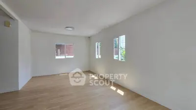 Spacious empty room with wooden flooring and natural light through windows.