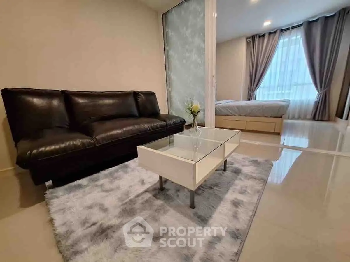 Modern living room with sleek black sofa and glass coffee table in open layout apartment.
