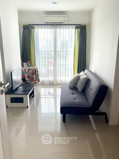 Cozy living room with modern sofa and TV, featuring bright natural light from large window.