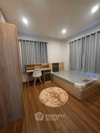 Modern bedroom with wooden flooring, stylish desk, and cozy bed setup.