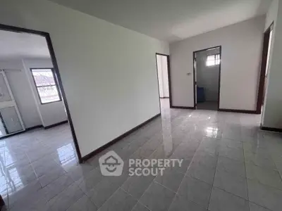 Spacious empty room with tiled flooring and multiple doorways in a well-lit home.