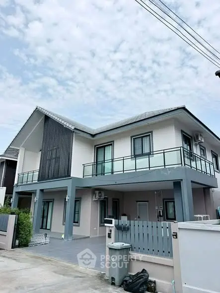 Modern two-story house with spacious balcony and sleek design under a clear sky.