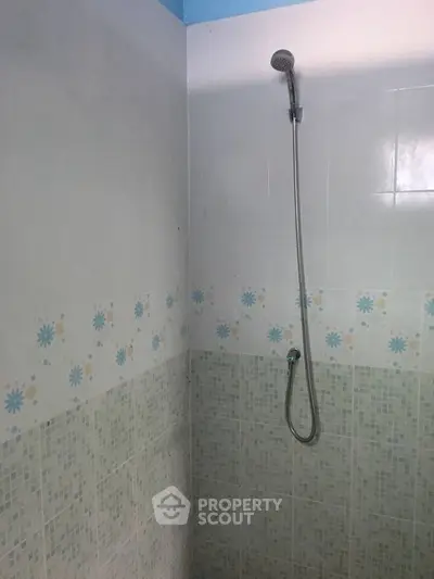 Simple bathroom with tiled shower area and handheld showerhead.