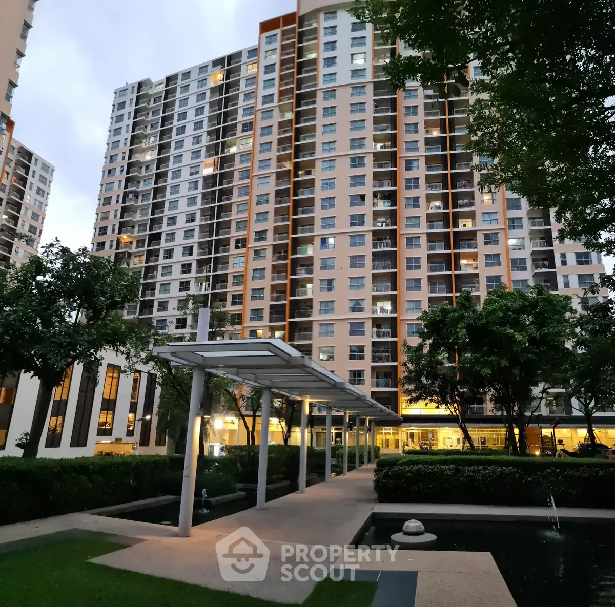 Modern high-rise apartment building with landscaped garden and walkway at dusk.