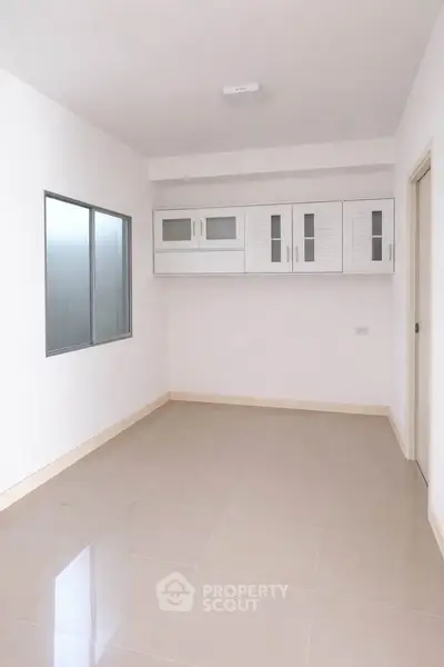Spacious empty room with tiled floor and modern white cabinetry, perfect for customization.
