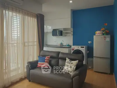 Modern living room with cozy sofa, balcony view, and compact kitchen featuring washing machine and fridge.