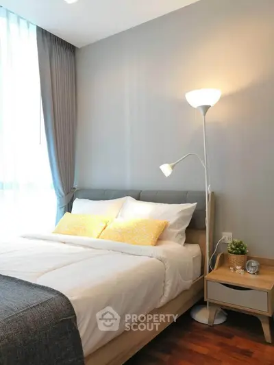 Cozy bedroom with modern decor and natural light, featuring a stylish floor lamp and elegant curtains.