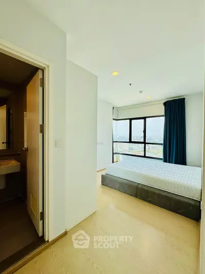 Bright bedroom with large window offering stunning city view, adjacent to modern bathroom.