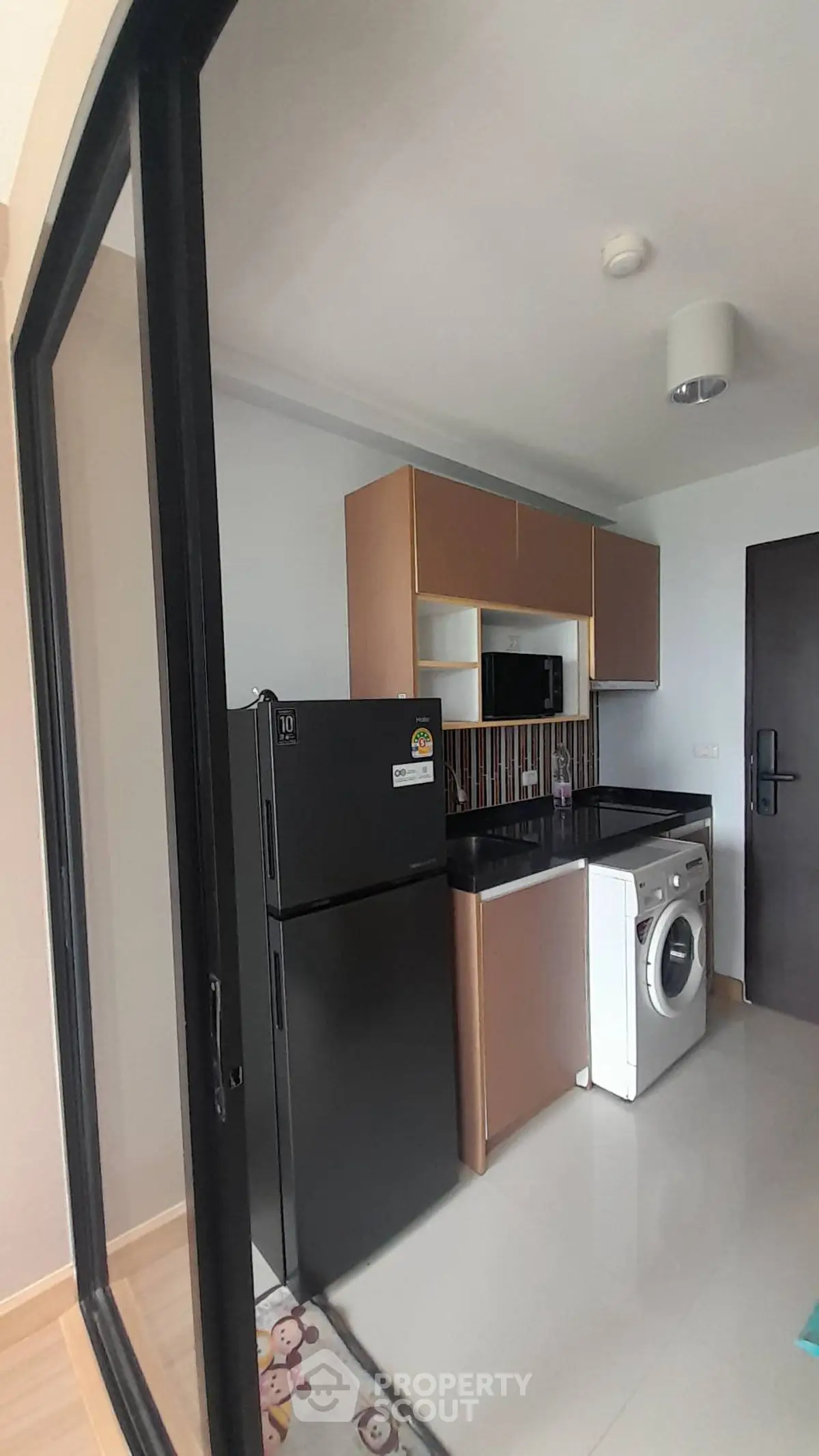 Modern compact kitchen with black fridge and washing machine in sleek apartment.