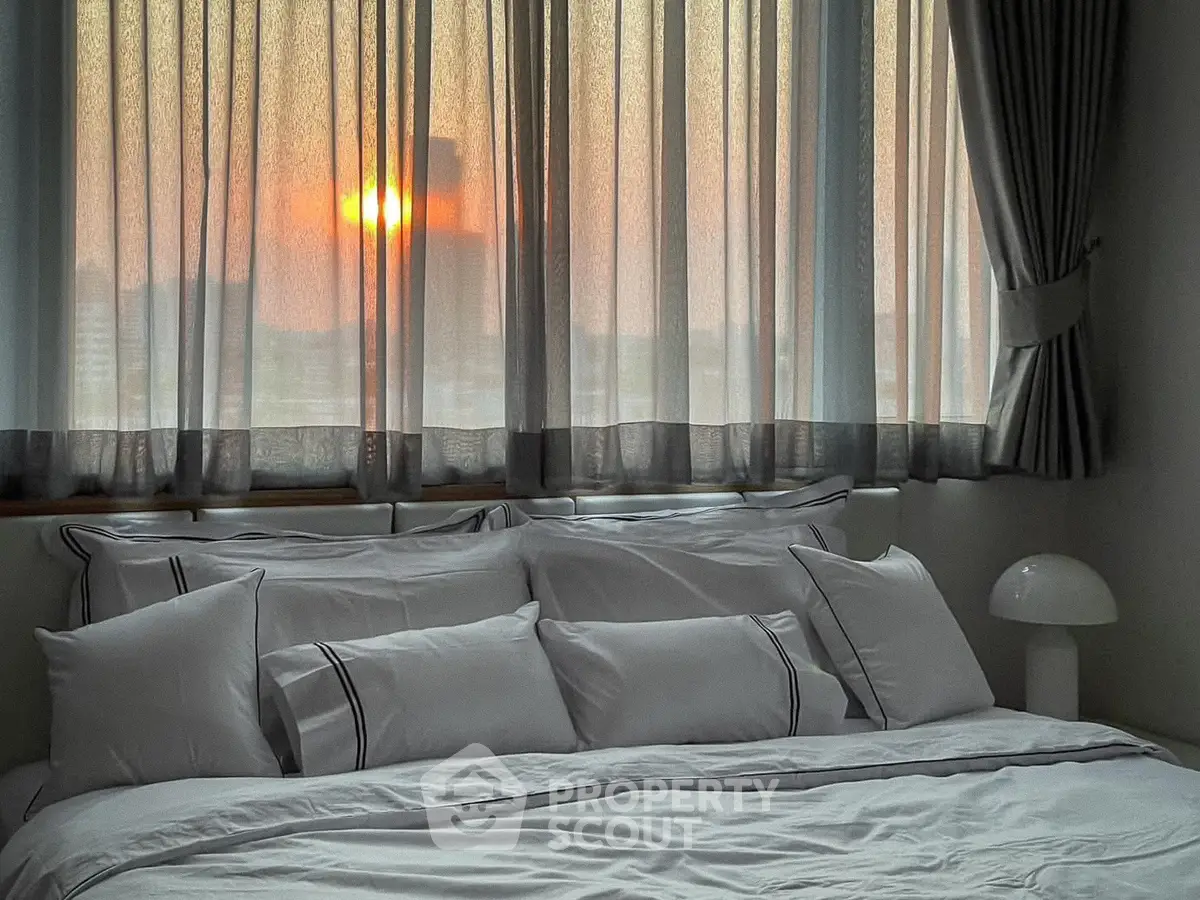 Cozy bedroom with elegant decor and stunning sunset view through large windows.