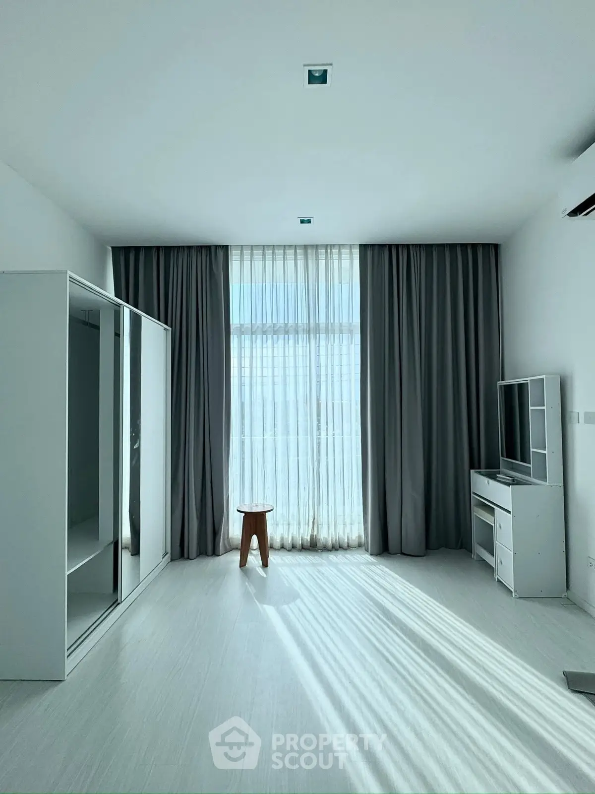 Spacious minimalist living room with modern furniture and large window drapes.