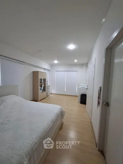 Spacious bedroom with modern decor and ample natural light, featuring sleek wooden flooring and minimalist design.