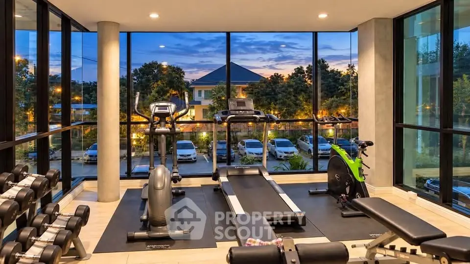 Modern gym with large windows offering scenic views, equipped with treadmills, exercise bikes, and weights.
