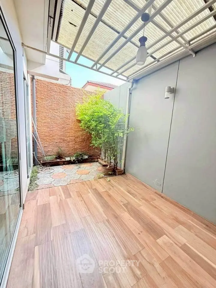 Charming small patio with wooden flooring and lush greenery, perfect for relaxation and outdoor enjoyment.