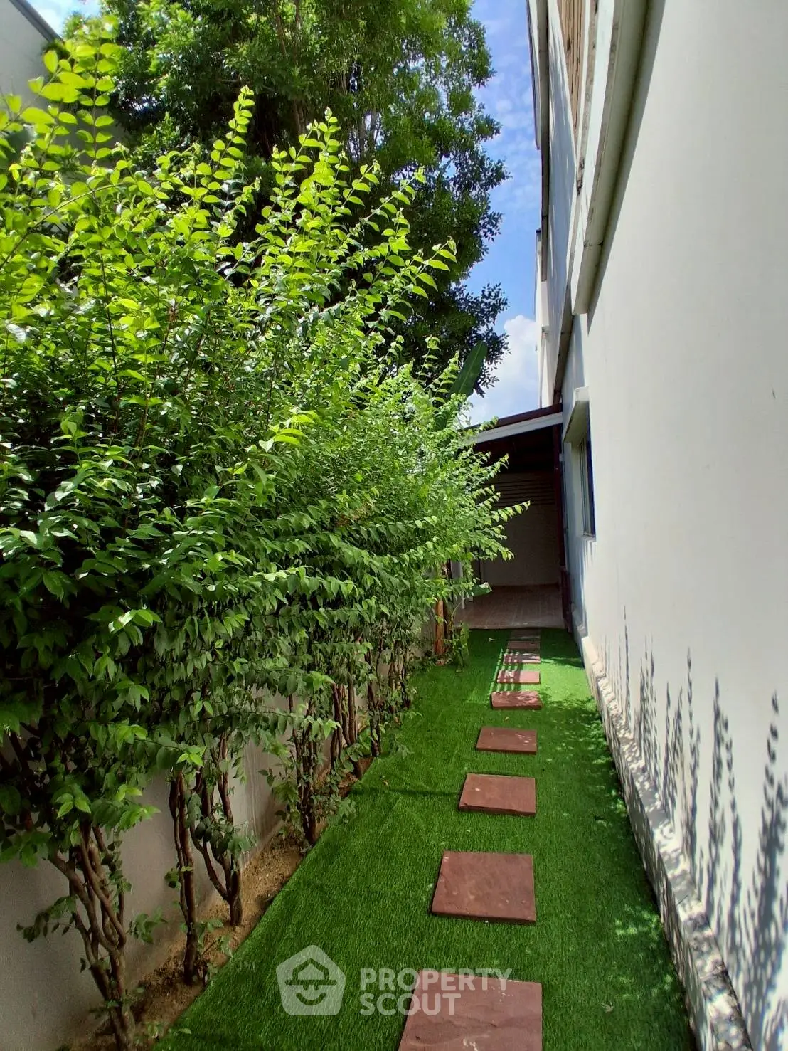 Charming garden pathway with lush greenery and stepping stones beside a modern building.