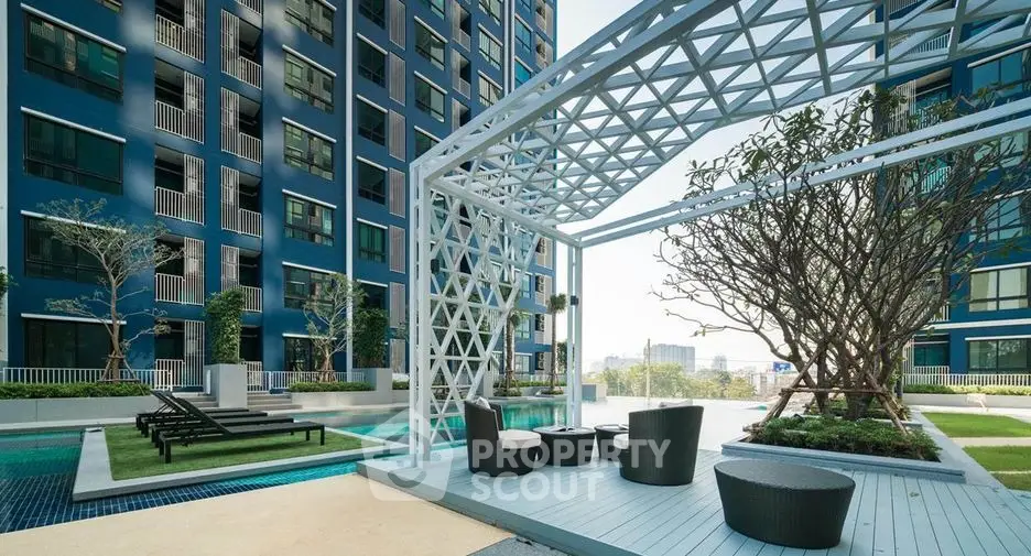 Luxurious modern apartment complex with poolside seating and lush greenery.