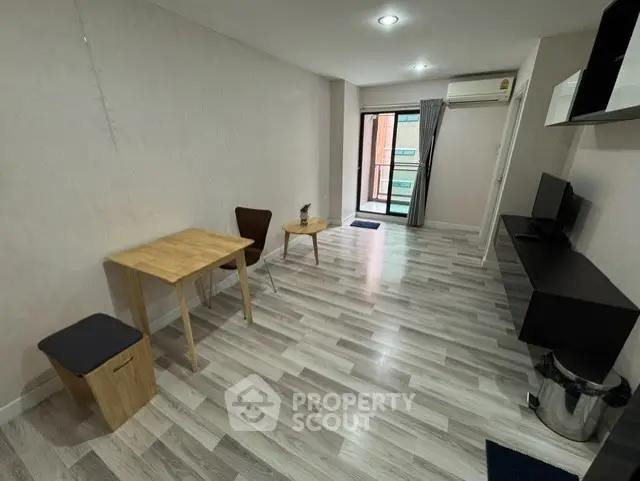 Modern living room with sleek flooring and minimalist furniture, featuring a small dining area and wall-mounted TV.