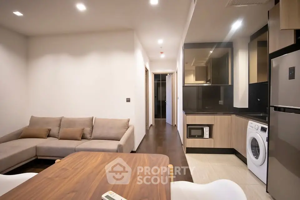 Modern living room with open kitchen, featuring sleek appliances and cozy seating area.