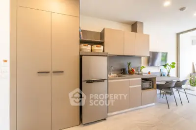 Modern kitchen with sleek cabinets and dining area, featuring a compact fridge and stylish decor.