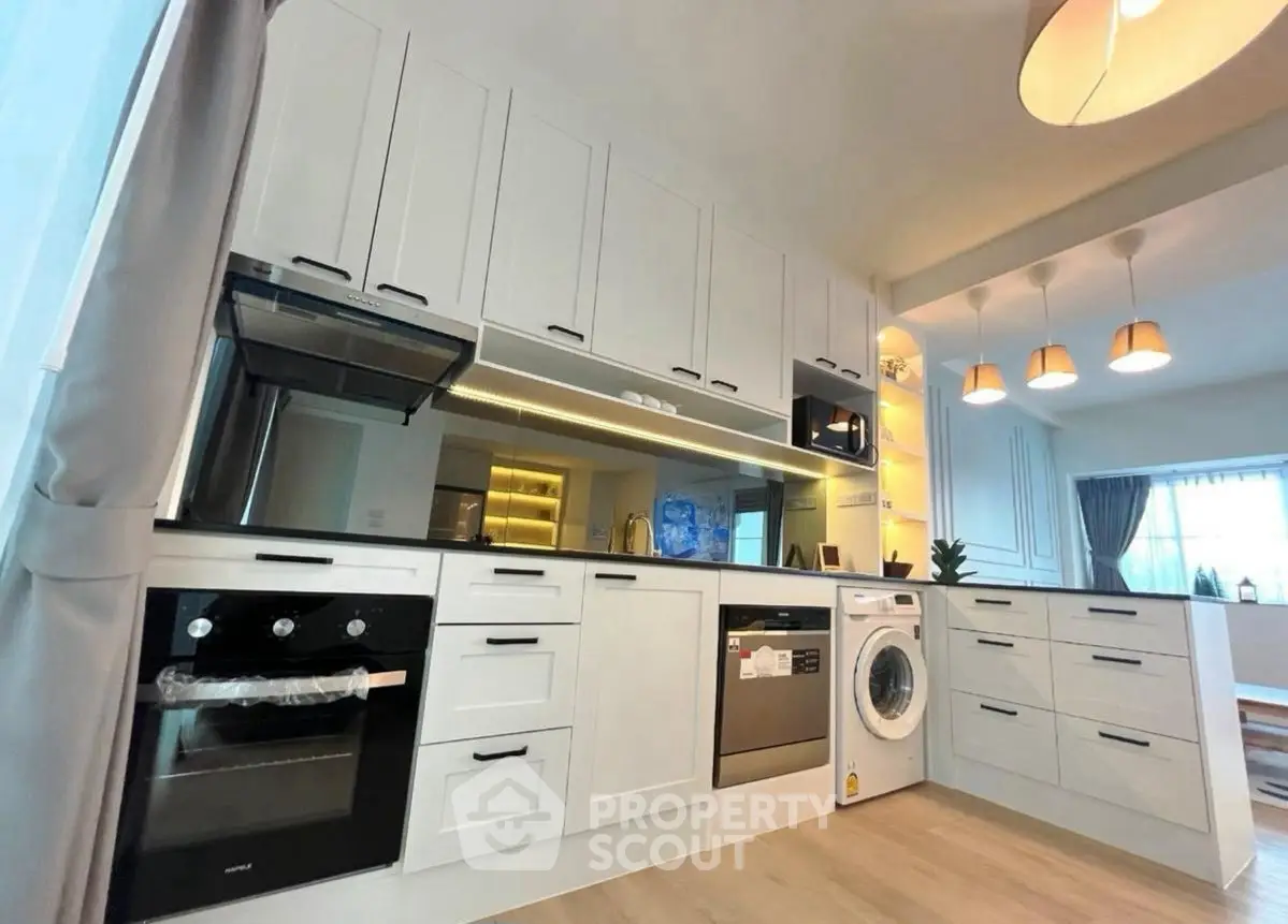 Modern kitchen with sleek white cabinets, built-in oven, and washing machine in open layout design.