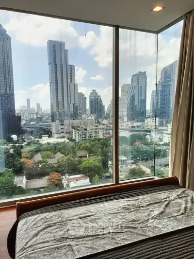 Luxurious bedroom with stunning city view through floor-to-ceiling windows in a high-rise apartment.