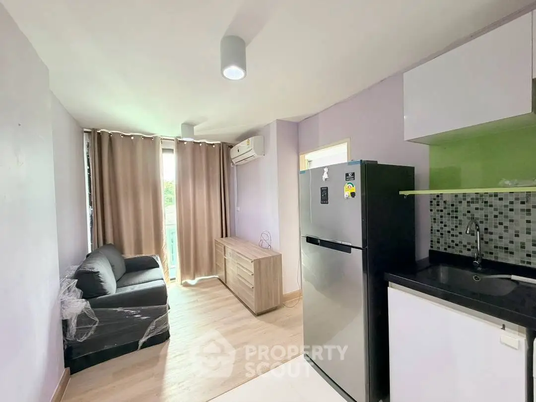 Modern living room with kitchenette, featuring a sleek fridge and cozy sofa, perfect for urban living.