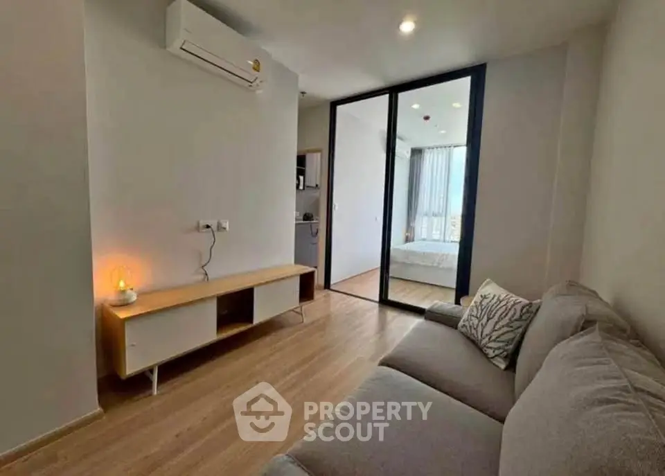 Modern living room with cozy sofa and sleek wooden flooring, featuring a view into a bright bedroom.