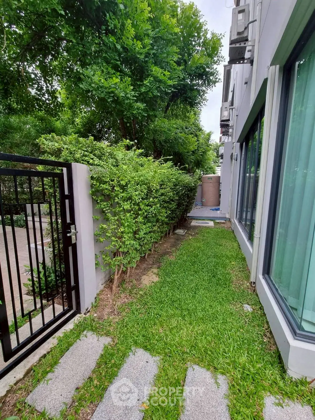 Charming garden path beside modern building with lush greenery and sleek gate