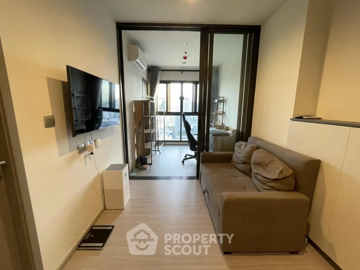Modern living room with cozy sofa and wall-mounted TV, leading to a bright study area with city view.