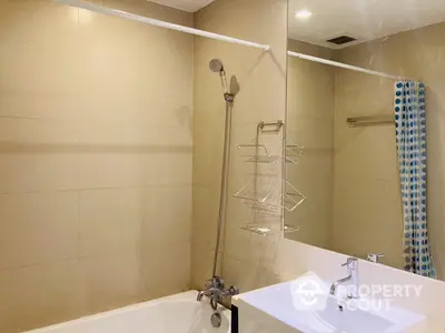 Modern bathroom with a full-sized tub, adjustable shower head, and a sleek sink, complemented by warm beige tiles for a cozy ambiance.