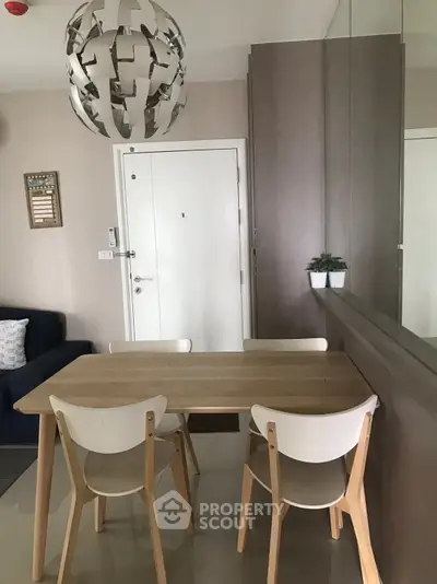 Modern dining area with stylish wooden table and chairs, featuring a unique pendant light and mirrored wall.