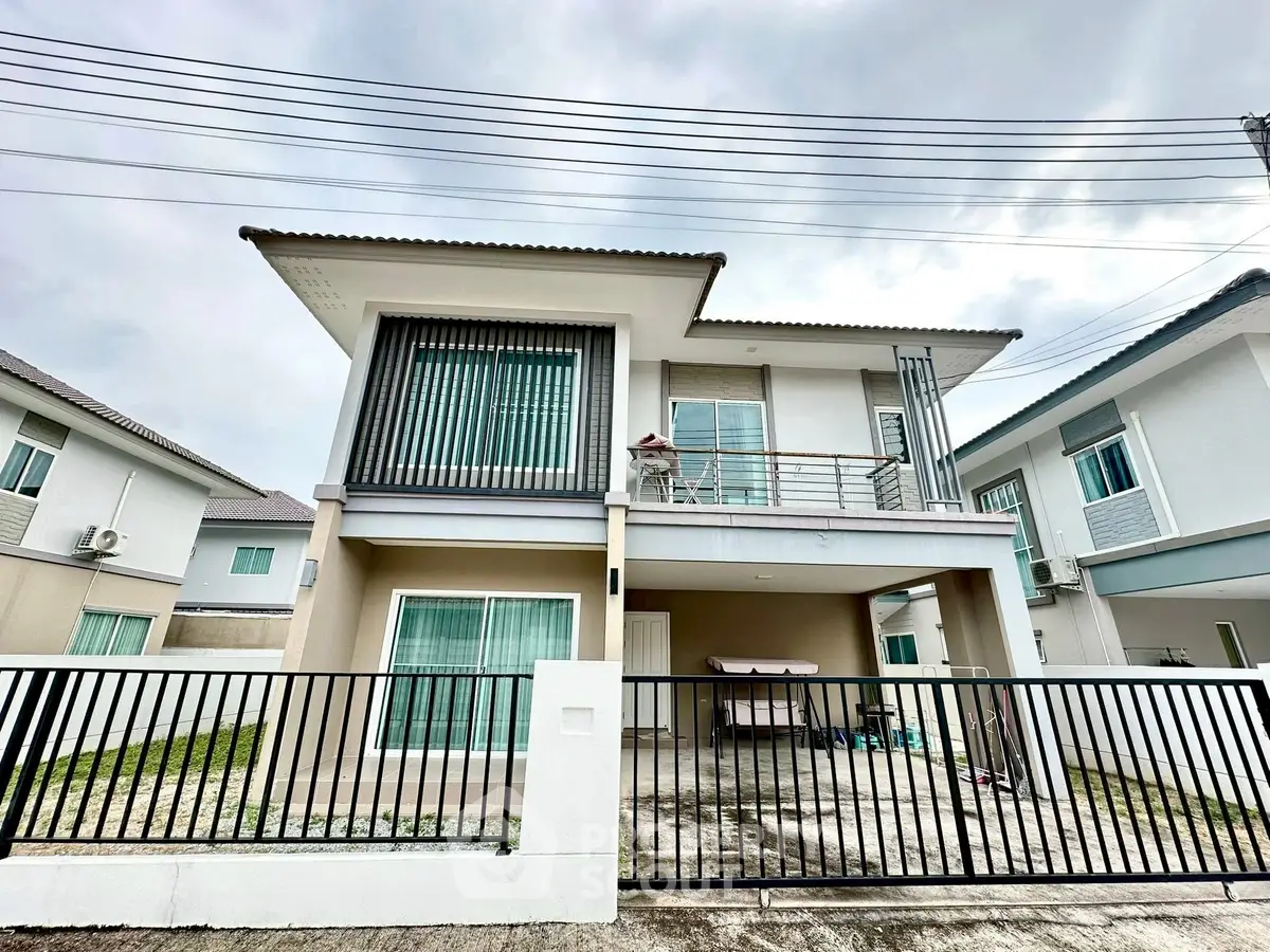 Modern two-story house with balcony and gated driveway in suburban neighborhood.