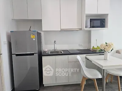 Modern kitchen with sleek appliances and minimalist design, featuring a fridge, microwave, and dining area.
