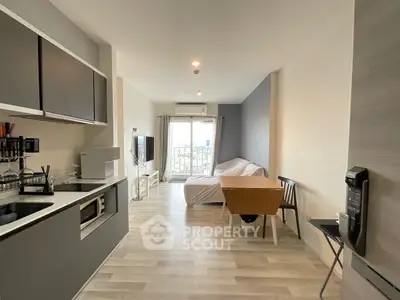 Modern open-plan studio apartment with sleek kitchen and cozy living area, featuring a large window with city views.