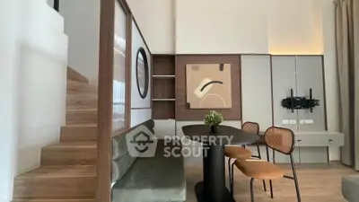 Modern living room with stylish decor and wooden staircase, featuring a cozy dining area and contemporary artwork.