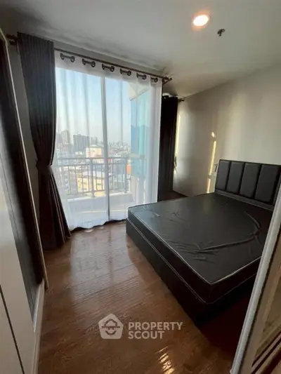 Modern bedroom with large window and city view, featuring sleek black bed and wooden flooring.